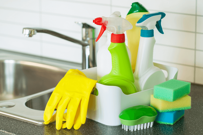 Cleaning supplies on a kitchen counter with a sink and a tile backsplash