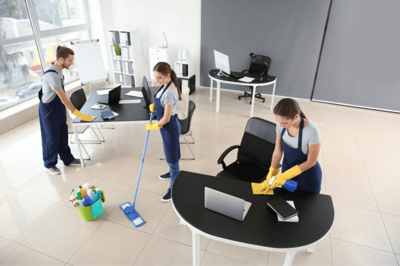 Three people cleaning an office space with blue uniforms and yellow gloves